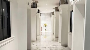 A hallway with white walls, marble flooring, and a decorative plant in the distance. - Hotel My Cang (Tra Vinh)