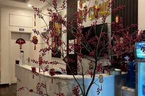 A reception area with a reception desk, a plant, and a television screen. - Hotel My Cang (Tra Vinh)