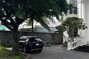 A black SUV parked in front of a building with a white staircase and a tree. - Hotel My Cang (Tra Vinh)