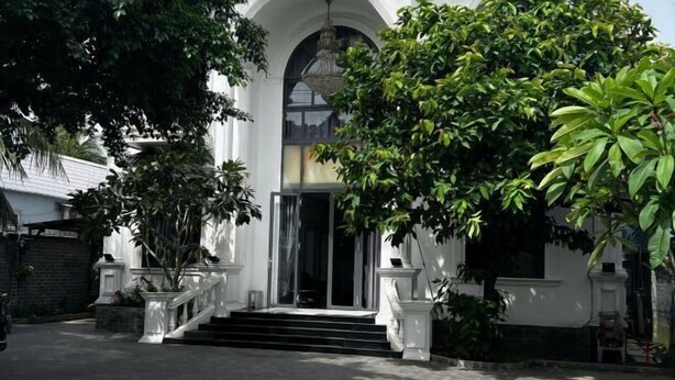 A building with a grand entrance, a staircase leading up to a door, and a large tree in front. - Hotel My Cang (Tra Vinh)