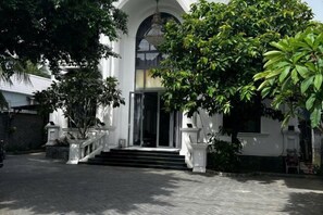 A building with a grand entrance, a staircase leading up to a door, and a large tree in front. - Hotel My Cang (Tra Vinh)