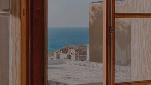 A view from a window with a wooden frame, overlooking a coastal area with buildings and the sea. - Chic 3BR Apt with Balcony, Mamad (Tel Aviv)