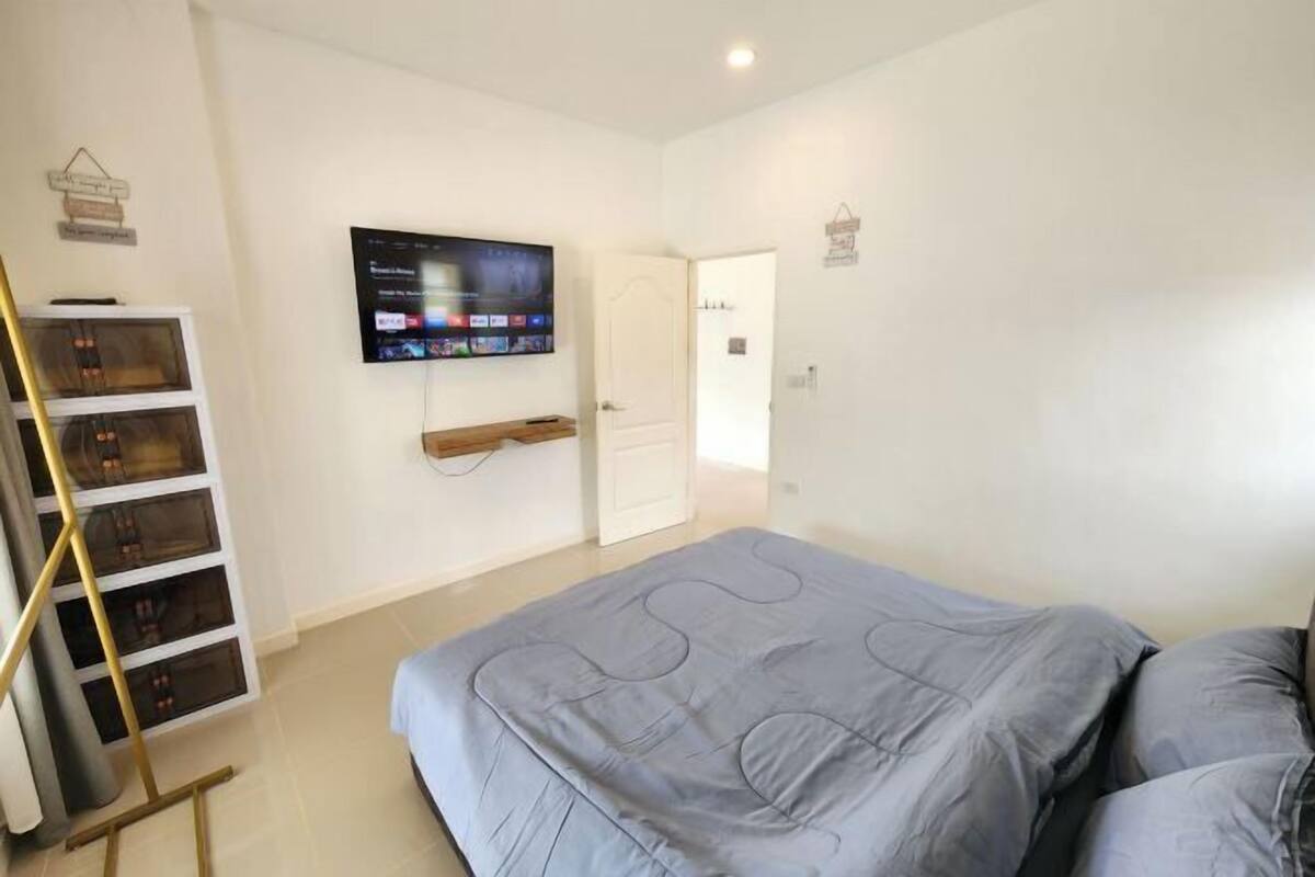 A bedroom with a bed, a television mounted on the wall, a wooden ladder, and a white door.