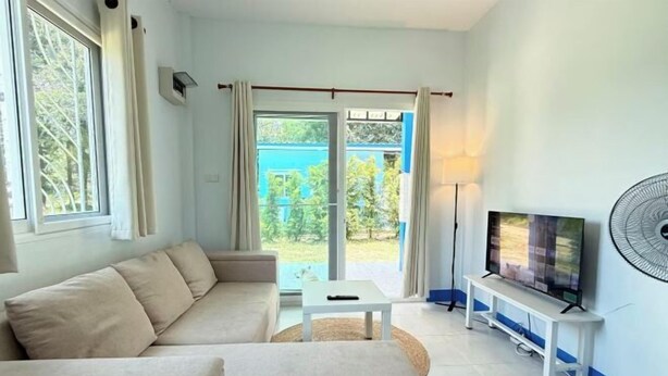 A modern living room with a sofa, a coffee table, a TV on a stand, and a fan. - Deniz’s Temple Light (Koh Phangan)