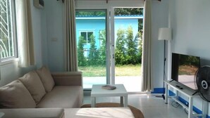 A living room with a sofa, a coffee table, a TV, and a sliding glass door leading to a balcony. - Deniz’s Temple Light (Koh Phangan)