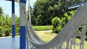 A hammock tied between blue and white pillars in an outdoor area with a view of greenery. - Deniz’s Temple Light (Koh Phangan)
