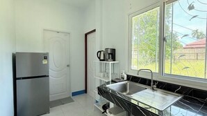 A compact kitchen with a refrigerator, a sink, and a window with a view of greenery. - Deniz’s Temple Light (Koh Phangan)