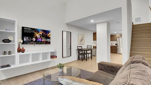 A modern living room with a flat-screen TV, a dining area, and a kitchen in the background. - Charming 1-bed loft, downtown Cleveland with GYM, Rooftop deck, Fire pit, games (Cleveland)