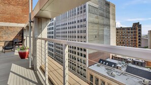A balcony with a view of a modern building, a potted plant, and a table with chairs. - Charming 1-bed loft, downtown Cleveland with GYM, Rooftop deck, Fire pit, games (Cleveland)