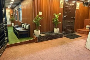 A reception area with a wooden wall, a sofa, two potted plants, and a door. - Rudhraksh Villa 4BR- Perfect Vacay Villa (Mussoorie)