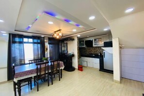A modern kitchen with a dining area, featuring a table and chairs, a refrigerator, and a microwave. - Rudhraksh Villa 4BR- Perfect Vacay Villa (Mussoorie)