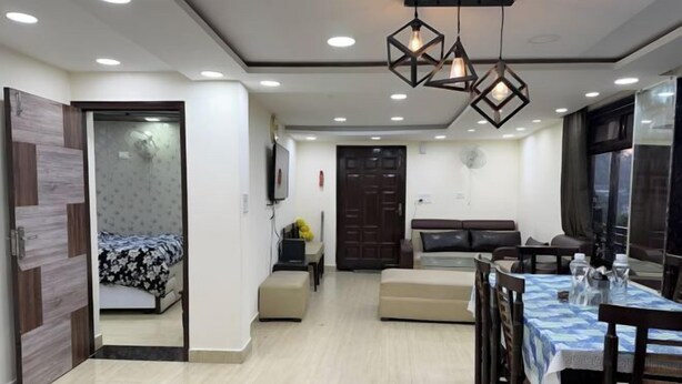 A modern living room with a sofa, a dining table with chairs, a TV, and a door leading to another room. - Rudhraksh Villa 4BR- Perfect Vacay Villa (Mussoorie)
