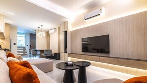 A modern living room with a flat-screen TV mounted on the wall, a sofa with orange cushions, and a coffee table. - P Villas Patong (Phuket)