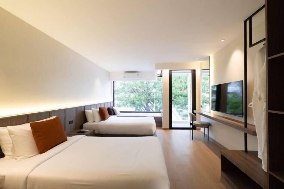 A modern hotel room with two beds, a TV, and a large window.