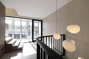 A modern interior with a staircase, pendant lighting, and a view through glass doors. - P Villas Patong (Phuket)