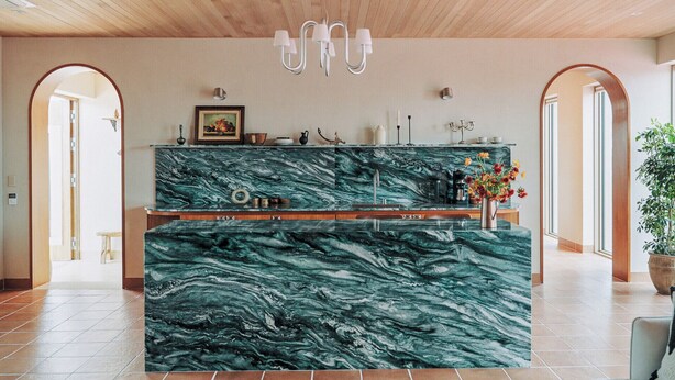 Een keuken met een marmeren aanrechtblad, houten plafond en een kroonluchter.