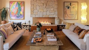 Een gezellige woonkamer met twee banken, een salontafel met boeken, een stenen open haard en kunstwerken aan de muur.