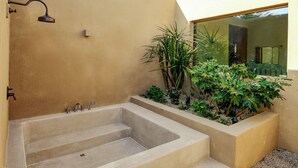Een moderne buitenbadkamer met een ruime badkuip, een trap die erheen leidt, en verschillende planten.