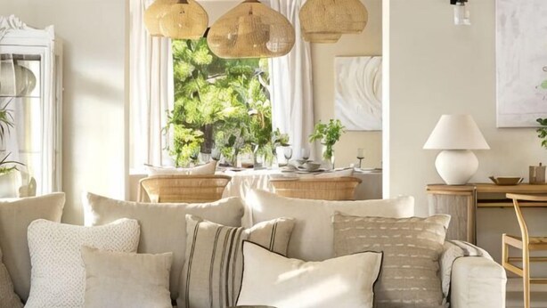 A living room with a sofa, cushions, a lamp, and a window with plants. - All About La Boheme (Benahavis)