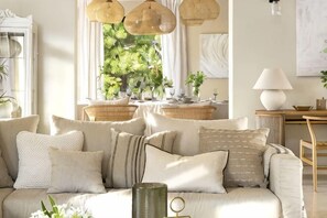 A living room with a sofa, cushions, a lamp, and a window with plants. - All About La Boheme (Benahavis)