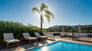 A swimming pool with lounge chairs and umbrellas, surrounded by greenery and a clear sky. - All About La Boheme (Benahavis)