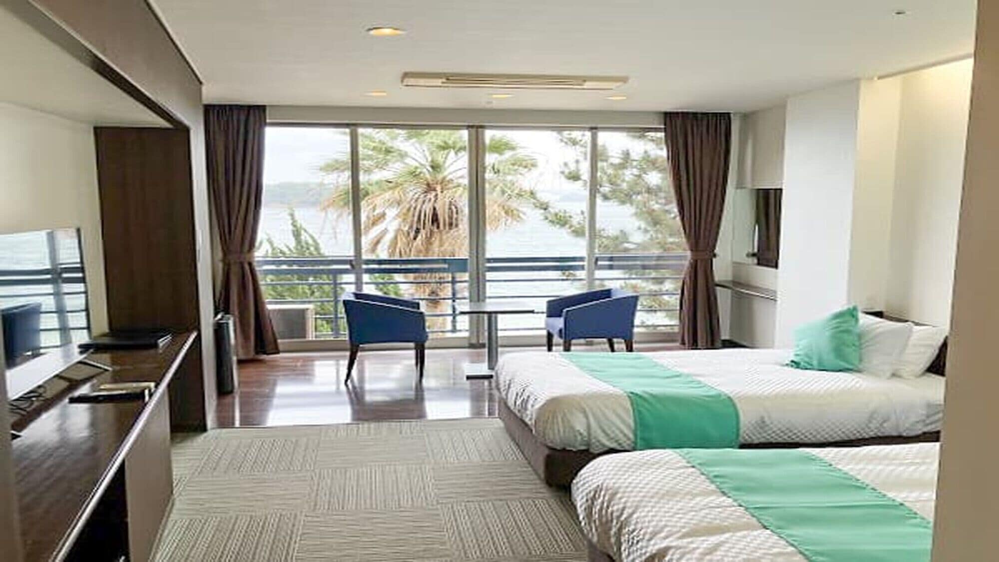 A hotel room with a balcony, a bed, a desk, and a chair.