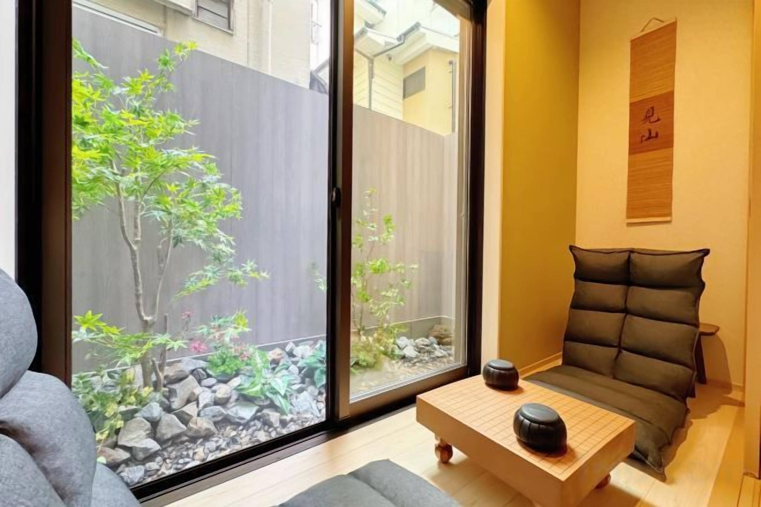 A room with a sliding glass door leading to a garden, a tatami mat seating area, and a small table with a bowl.