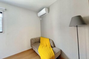 A room with a sofa, a lamp, and an air conditioning unit. - EI・RIN (Osaka)