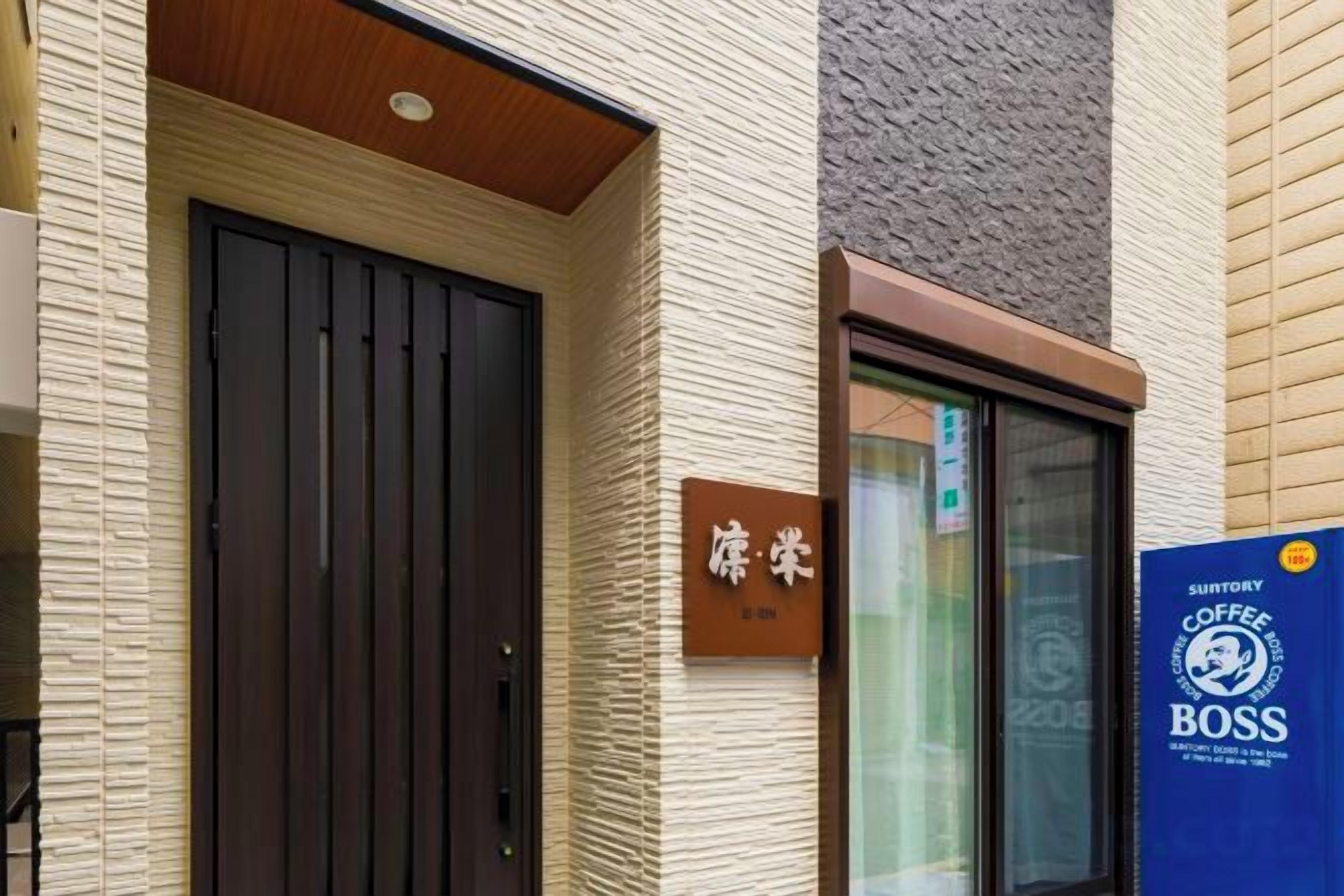 Fachada de edificio con una puerta marrón oscuro, una ventana y un letrero con caracteres japoneses.