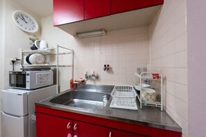 A kitchen with a stainless steel sink, red cabinets, a microwave, and a clock on the wall. - Febbraio Namba appartamento (Osaka)