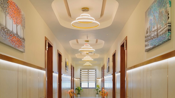 A hotel corridor with a polished floor, wooden doors, and potted plants. - Hotel Saubhagya Ahmedabad (Ahmedabad)