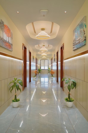 A hotel corridor with a polished floor, wooden doors, and potted plants. - Hotel Saubhagya Ahmedabad (Ahmedabad)