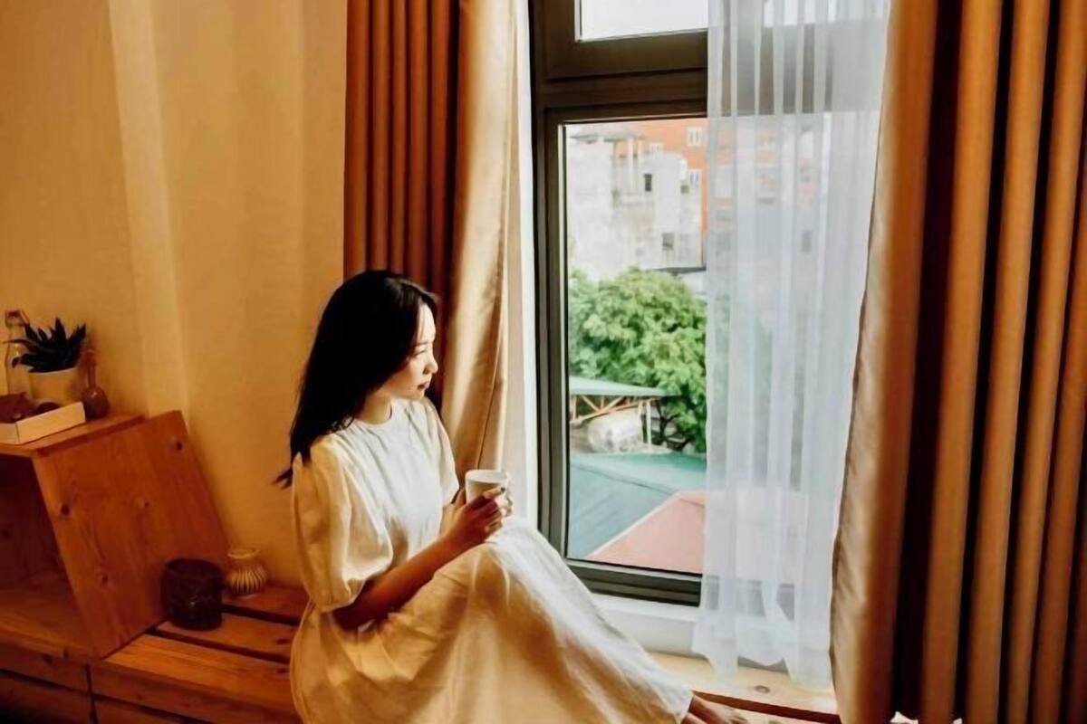 A person sitting by a window with curtains, holding a cup.