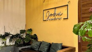 Un mur jaune sur lequel est accroché un panneau encadré portant l’inscription « Jodevi Homestay ».