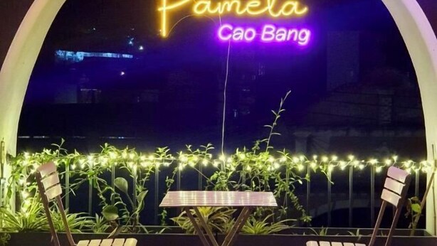 Une enseigne au néon portant l’inscription « Pamela Cao Bang » surplombe une table entourée de chaises, le tout étant agrémenté de plantes et de guirlandes lumineuses.