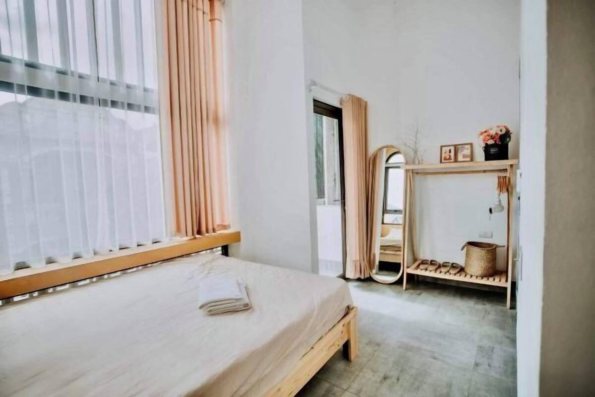 A bedroom with a bed, a mirror, a shelf with shoes, and a window with curtains.