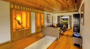 A hallway with wooden flooring, a wicker sofa, a rug, and a display cabinet with illuminated items. - Pa Sak Tong (Chiang Rai)