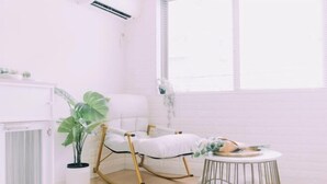Une pièce avec un fauteuil à bascule blanc, une petite table ronde avec une plante, et une plante en pot placée à côté du fauteuil.