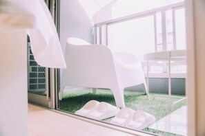 Un intérieur moderne avec des chaises blanches et une porte vitrée donnant sur un espace extérieur avec de la pelouse.