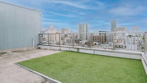 Une terrasse sur le toit, avec une pelouse verdoyante, une rambarde en métal et une vue sur les toits de la ville en arrière-plan.