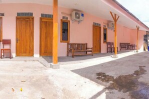 A building with multiple wooden doors, a covered porch with benches, and a concrete ground. - Wahyu Putri House Yogyakarta (Kraton)