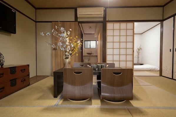 A traditional Japanese room with tatami flooring, a low table with cushions, and a sliding door leading to a bedroom.