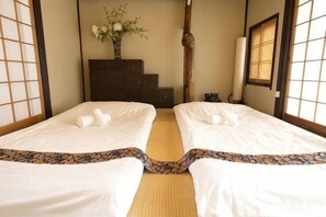 A traditional Japanese room with tatami flooring, two beds with white bedding, a dark wooden dresser, and a vase with flowers. - KIRAKU･SHIMIZU (Kyoto)