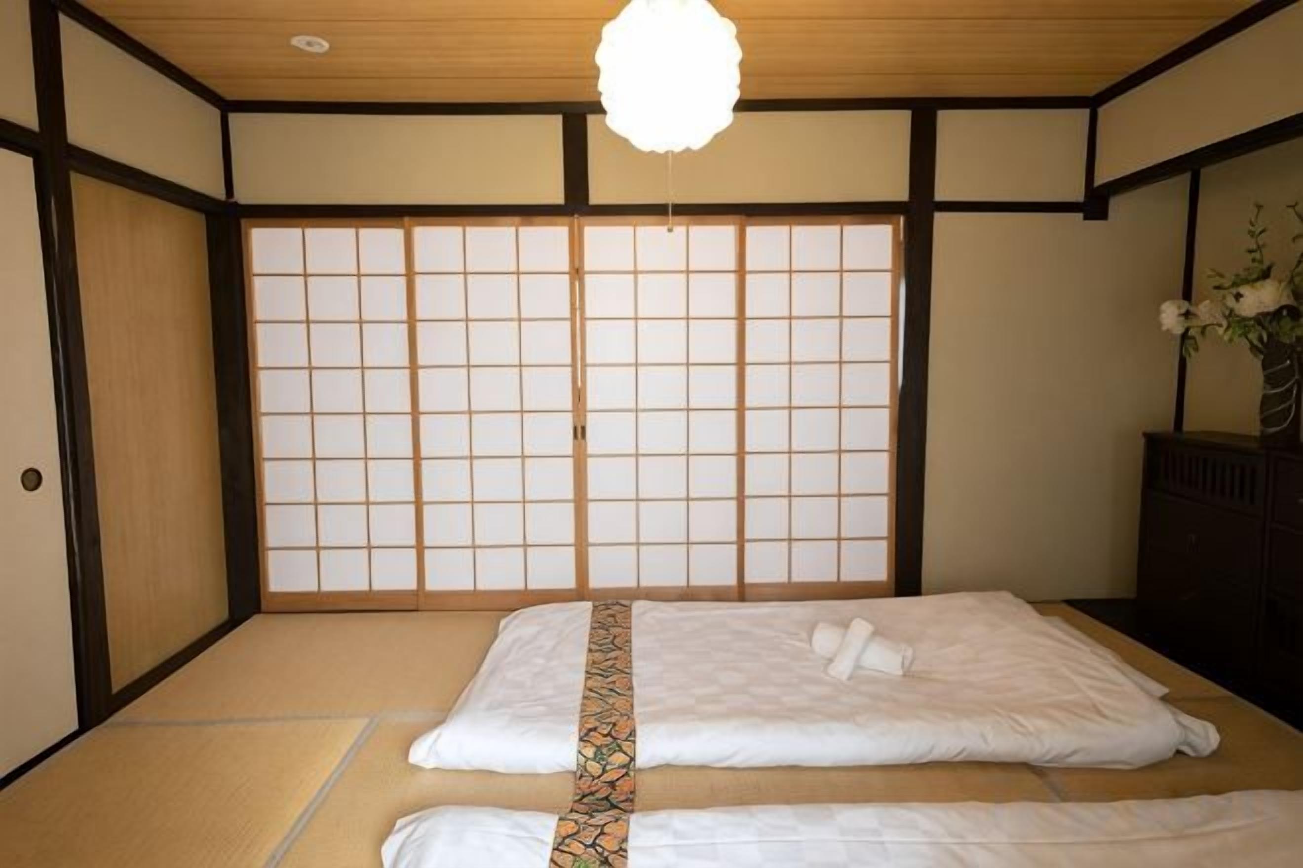 A traditional Japanese-style room with tatami flooring, a shoji screen wall, and a bed with white bedding.
