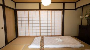 A traditional Japanese-style room with tatami flooring, a shoji screen wall, and a bed with white bedding.