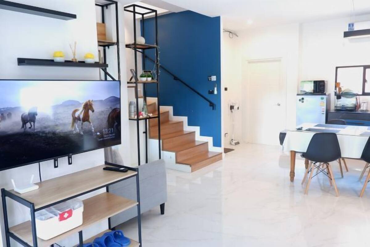 Un salon moderne doté d’un téléviseur à écran plat, d’un escalier et d’un coin repas avec une table et des chaises.