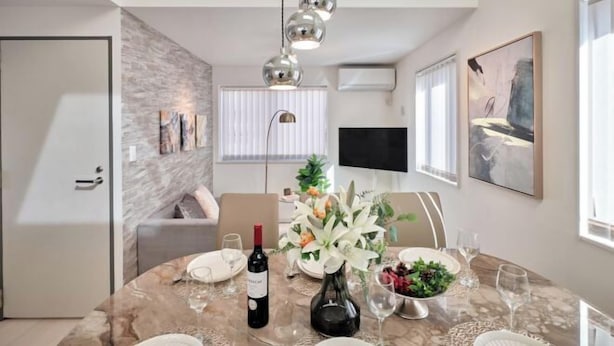A dining area with a marble table, wine bottle, flowers, and a TV in the background. - 1 stop to Shinjuku 13 min to Shibuya Private house rental LUXU Urban Shinjuku (Tokyo)