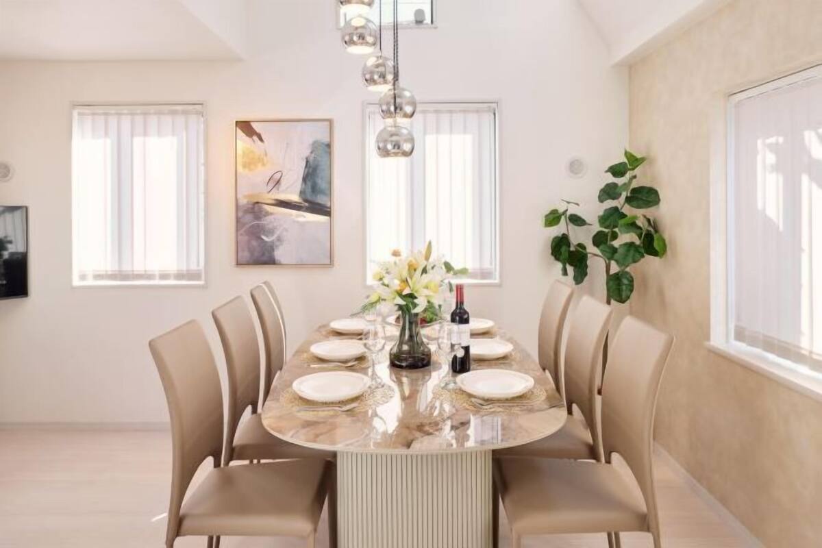 A dining area with a marble table, beige chairs, a vase with flowers, and a painting on the wall.