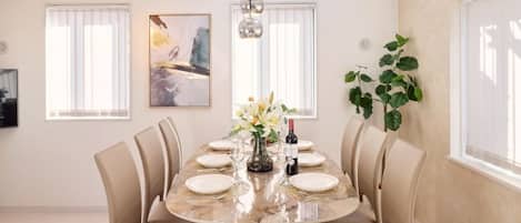 A dining area with a marble table, beige chairs, a vase with flowers, and a painting on the wall.