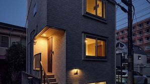 A modern two-story building with a brick facade and illuminated windows at dusk. - 1 stop to Shinjuku 13 min to Shibuya Private house rental LUXU Urban Shinjuku (Tokyo)